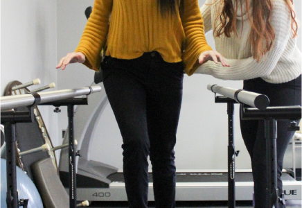 A physical therapist assisting a patient with walking exercises during workers' comp physical therapy using parallel bars